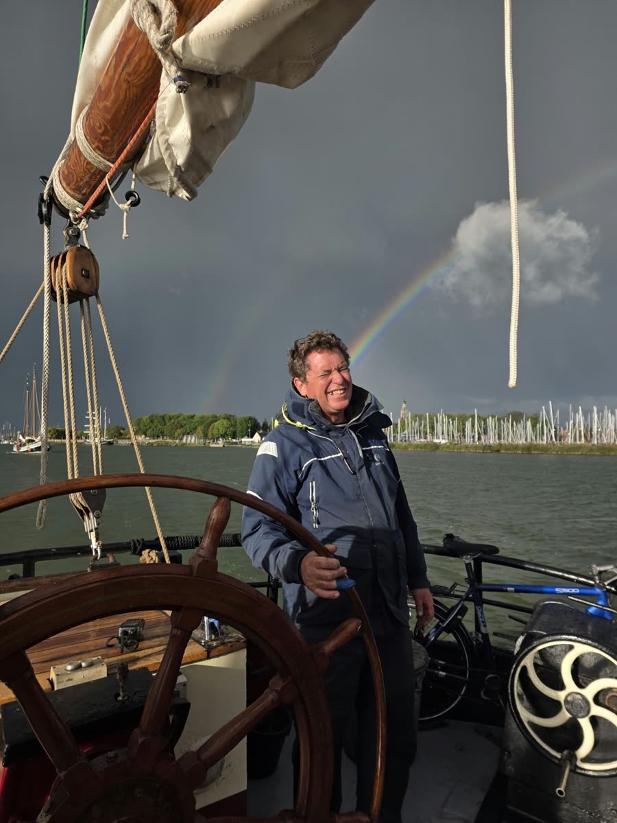 Schipper Laurens Sinaasappel aan het roer van de Johanna Engelina, met een dubbele regenboog boven de haven